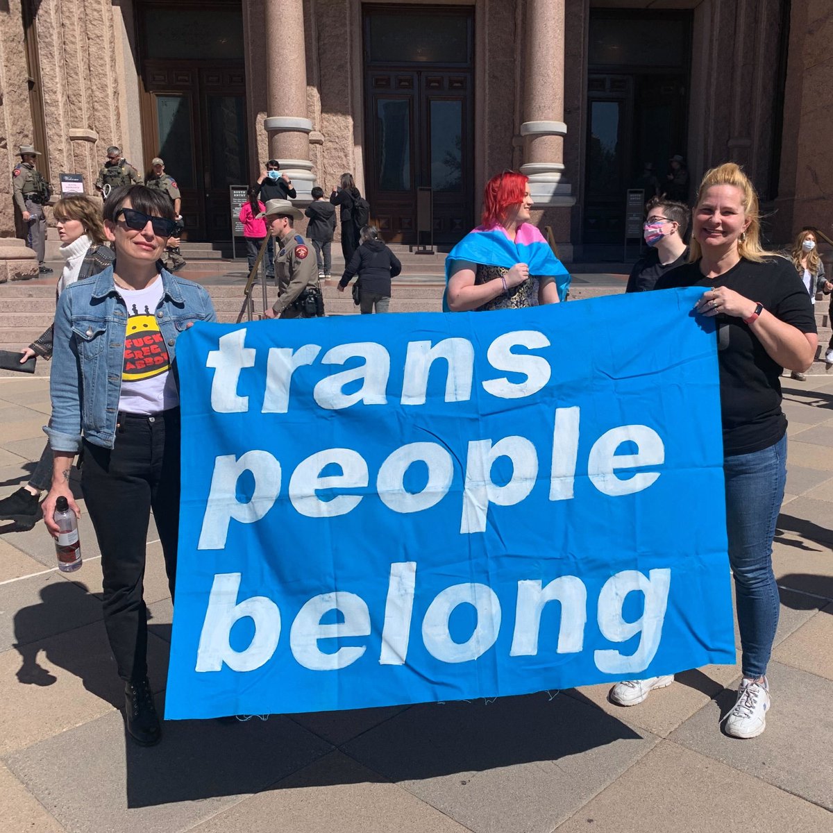 Two people holding a sign that reads "trans people belong"in front to the state capitol. Photo credit: Nick Hudson