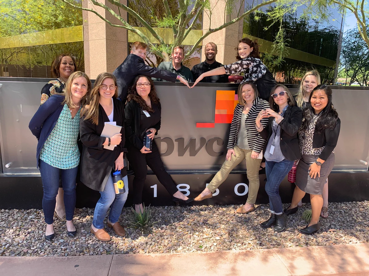 A team of employees poses with the PwC sign outside of an office.