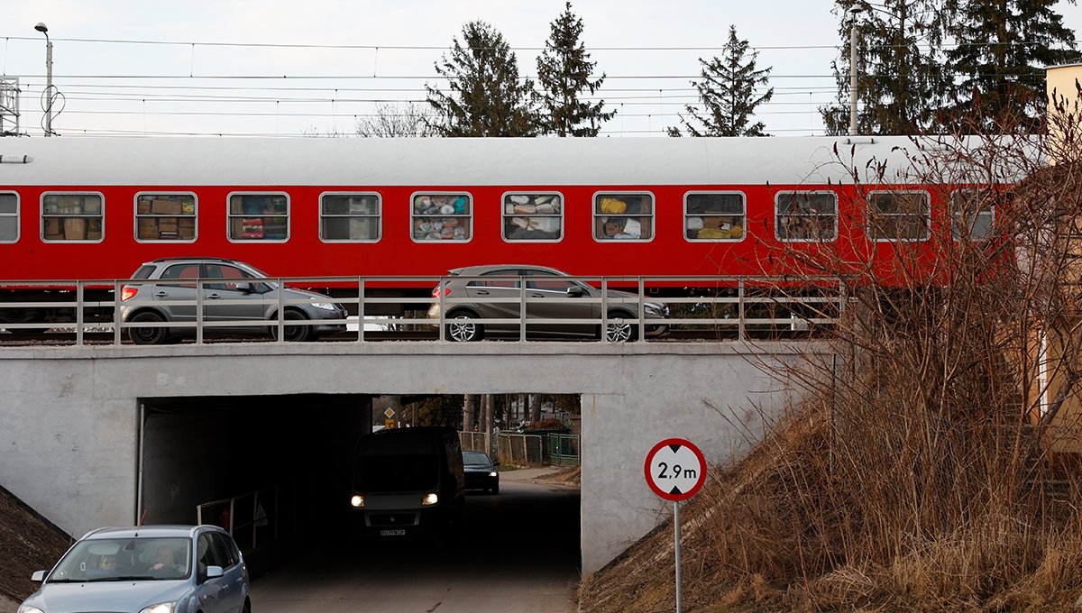 Auf dem Bild ist ein roter Zug zu sehen. Er fährt über eine Brücke. Im Vordergrund Autos. Durch die Fenster des Zuges sieht man unzählige Kartons und andere Gegenstände, die dort gestapelt wurden.