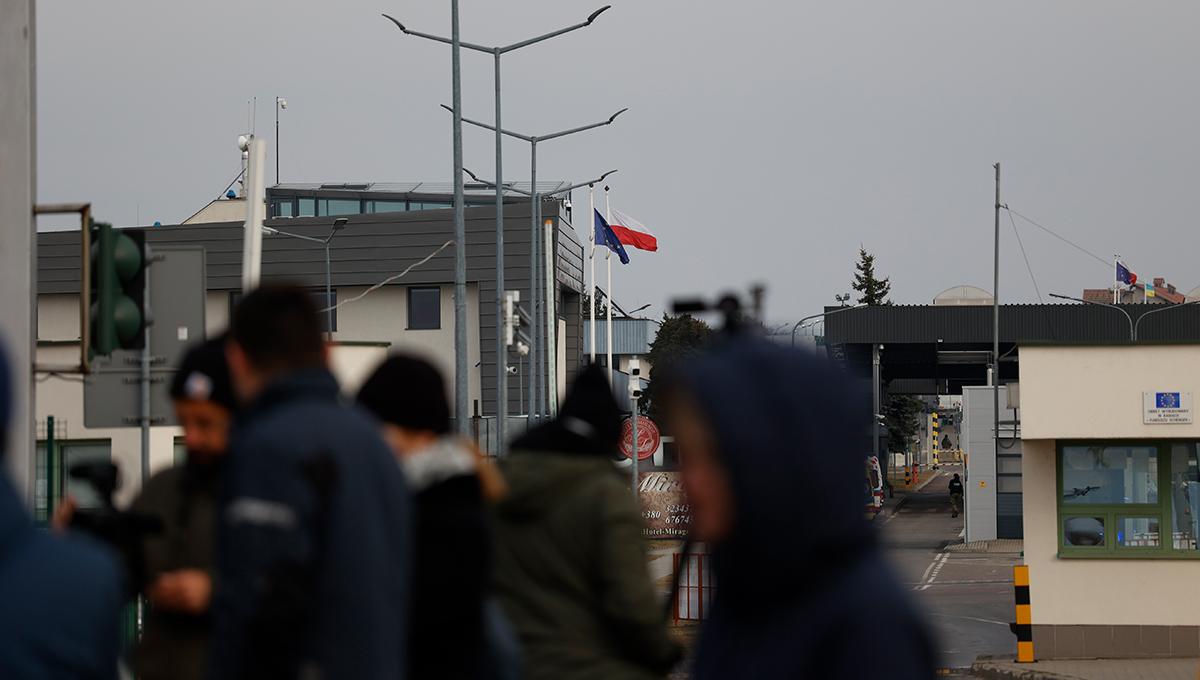 Das Bild zeigt mehrere Gebäude an der polnisch-ukrainischen Grenze. Im Vordergrund verschwommen einige Menschen.