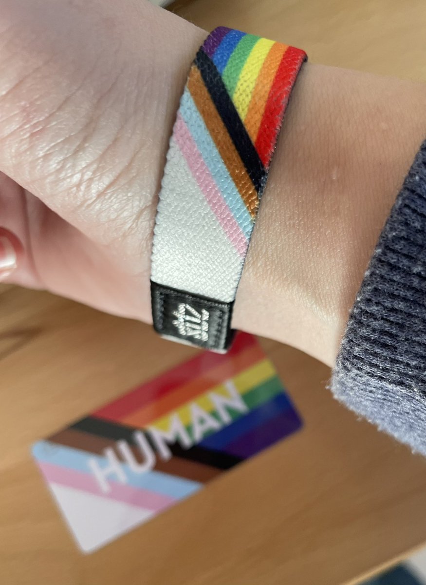 Photo of my wrist wearing the ZOX wristband. It is striped with the colours of the progress pride rainbow flag.