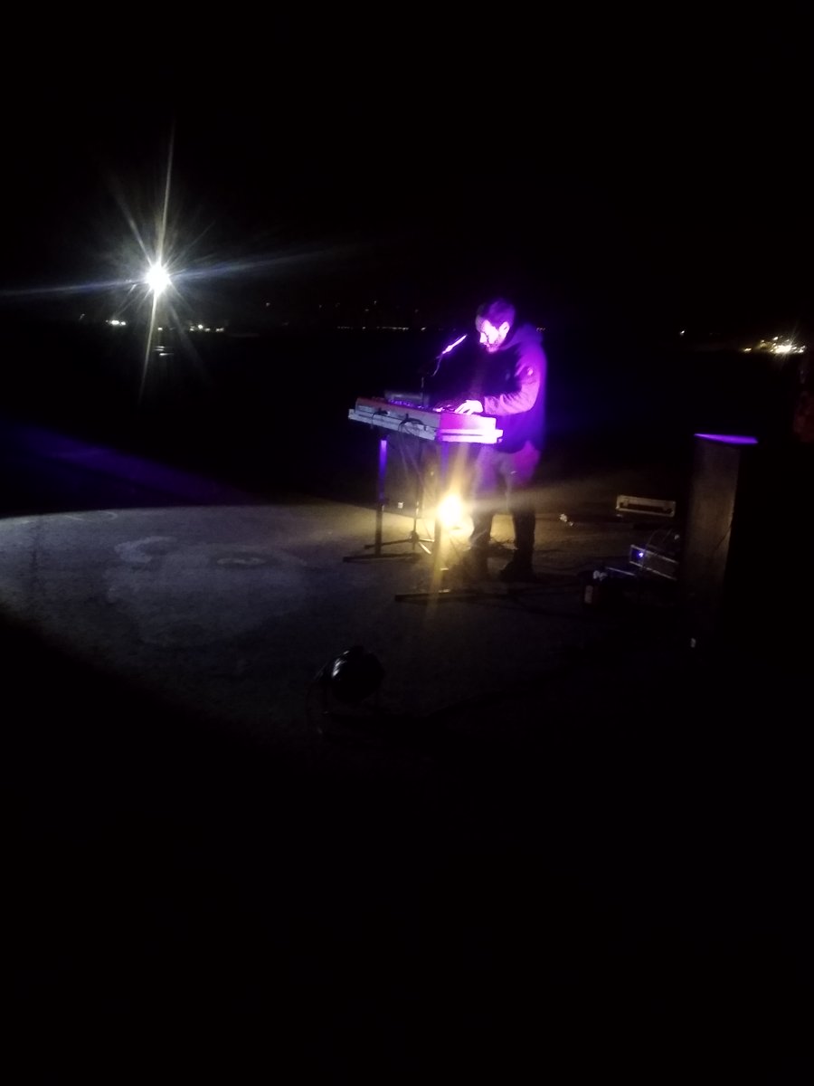 Enno Bunger im lila Licht der Leuchtschau getaucht bei seinem Konzert in Lützerath an der Mahnwache vor der Grube. Die Erkennbaren Lichter im Hintergrund stammen von den Maschinen in der Kohlegrube.