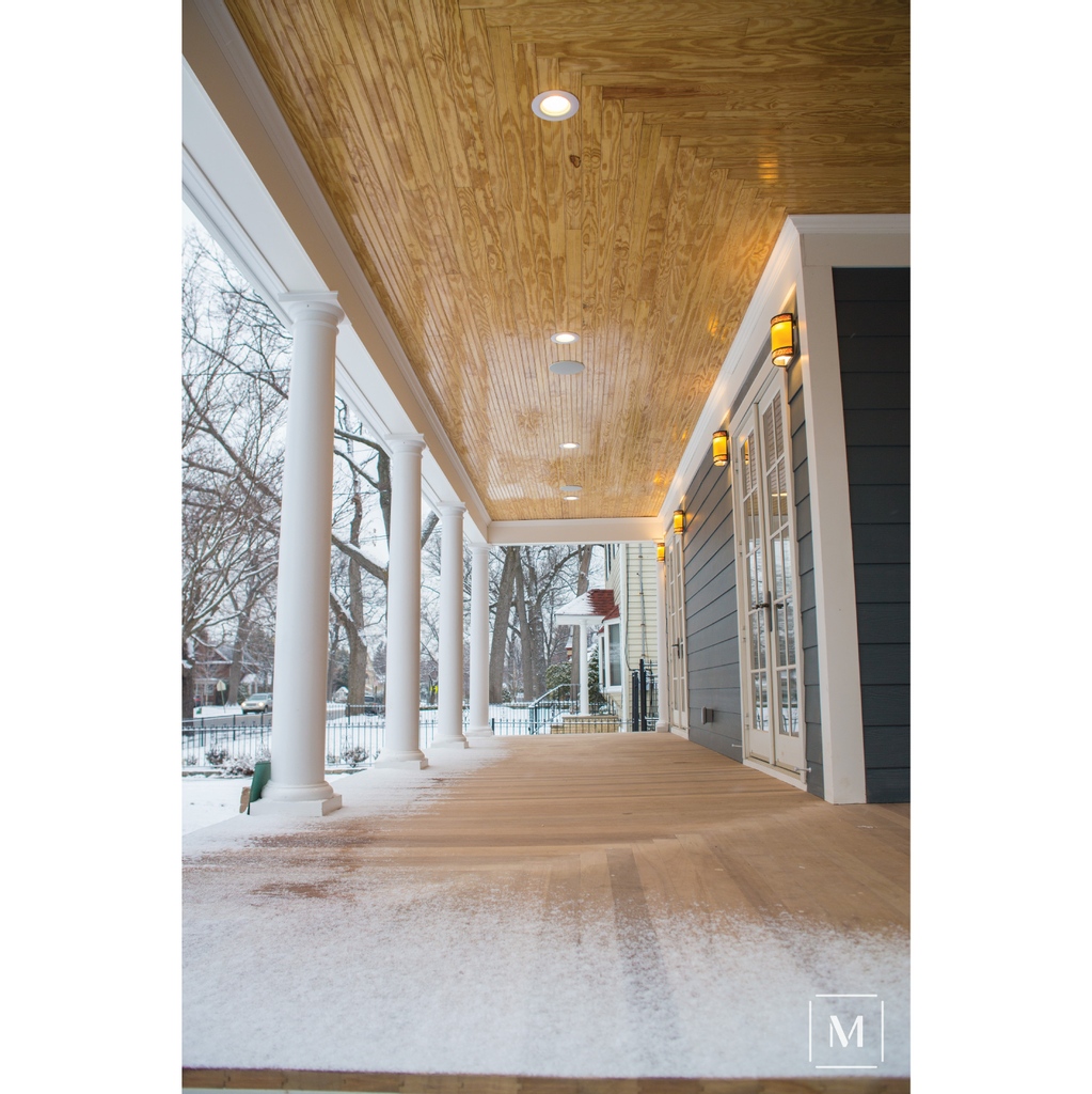 This porch renovation adds dimension and character with the natural mahogany wood porch planks and a beadboard ceiling that contrasts with the navy plank siding.