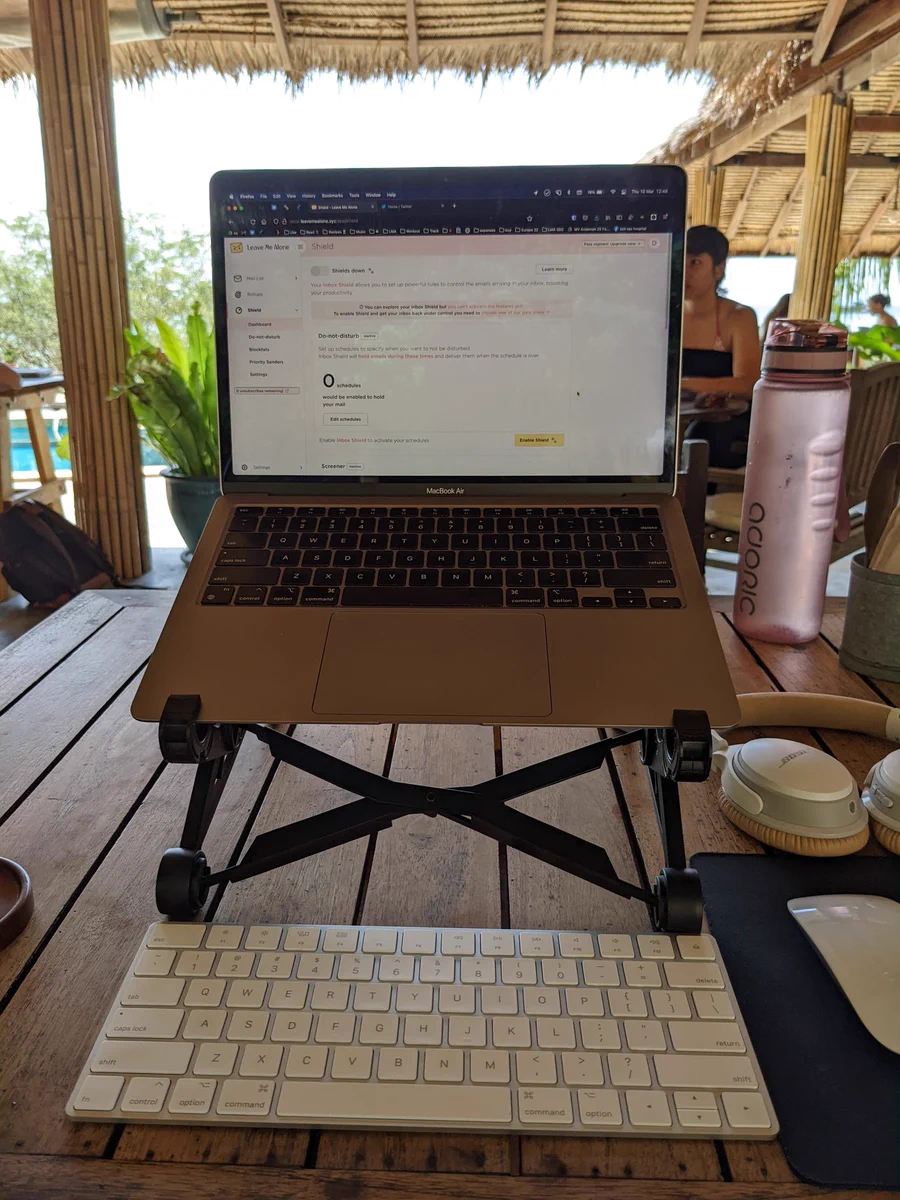 Mac laptop on a stand with wireless keyboard, mouse, and headphones on a cafe table