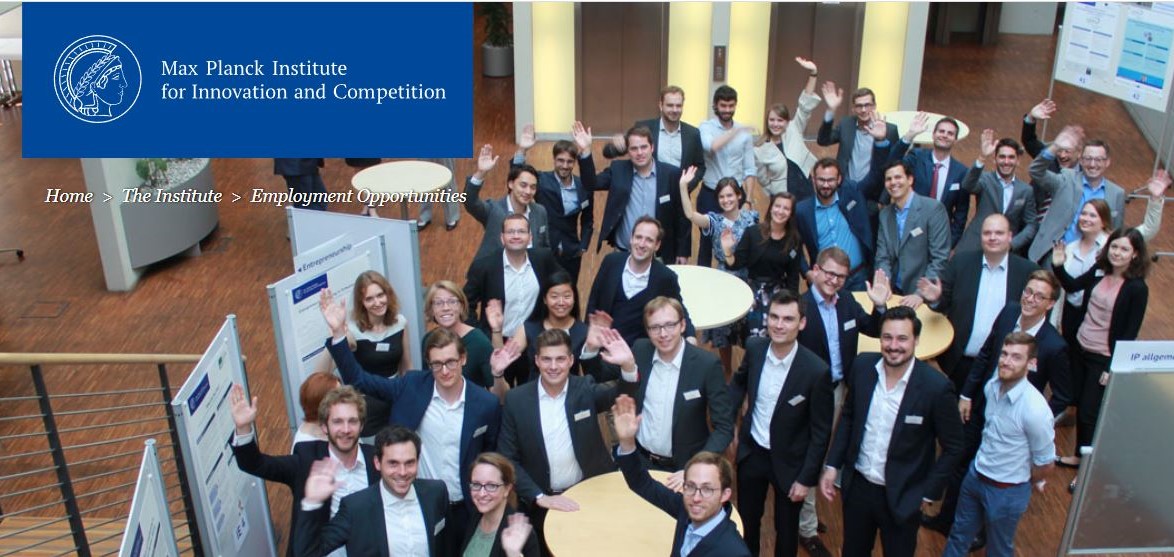 A group of smiling and waving young researchers during a poster presentation in the grand hall of the Max Planck Institute for Innovation and Competition in Munich, Germany.