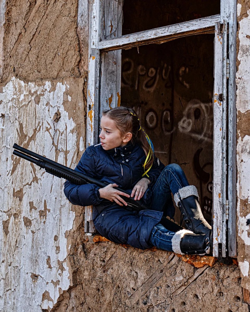 Incredible photo of a Ukrainian girl (taken by her father) posing with her dad's gun, with yellow and blue ribbons in her hair, sucking a lollipop. As a dad this touches me so deeply. War doesn't happen to countries, it happens to people, including kids. 💛💙#IStandWithUkraine️