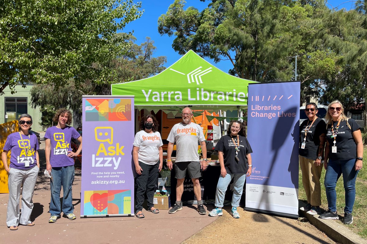 Group photo of Staff from Ask Izzy/Infoxchange, Orange Sky and Yarra Libraries smiling in front of Yarra Libraries and AskIzzy banners