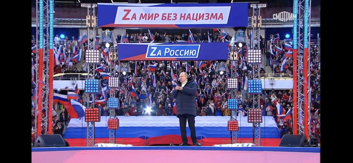 Here’s Putin. He seems to be on his own special giant stage so nobody can get within 20 yards of him even in a massive stadium.The sings behind him say “For a world without Nazism / For Russia”