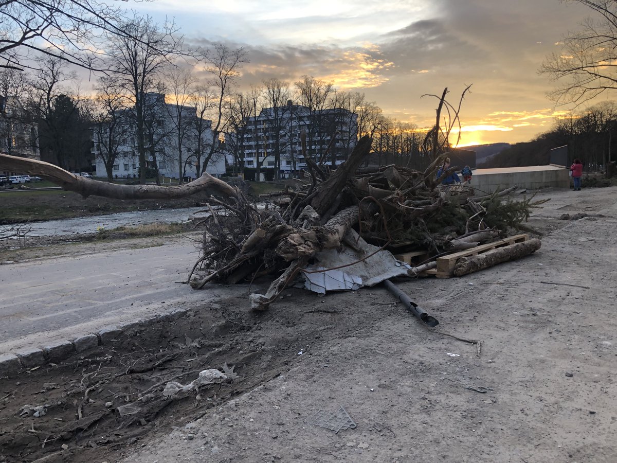 Im Hintergrund der Abendhimmel, im Mittelgrund ein großer Haufen Treibholz mit Stämmen, Ästen, Zweigen, im Vordergrund Wege, die von Staub bedeckt sind. Ufer in Bad Neuenahr.