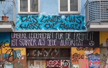 Foto vom Hauseingang der Rigaer Straße 94. Über dem Portal steht geschrieben:
"Das ganze Haus hasst die Polizei!" &
"Unsere Leidenschaft für die Freiheit ist stärker als jede Autorität!"