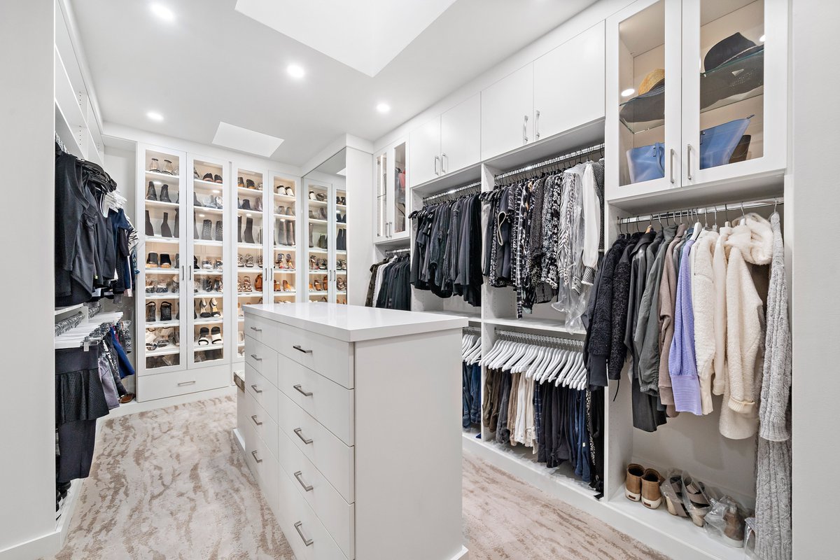 A well-lit elegant closet anyone? With a silky-smooth white finish, you'll love waking up to this every morning and walking past satin nickel pulls, adjustable glass shelving and a beautifully placed seating area next to a wall of heels! Free consultation: bit.ly/3CU3ADN