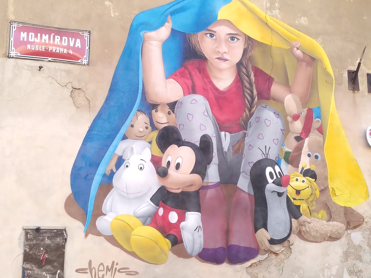 Ein Mädchen sucht mit Plüschtieren wie der Biene Maja und dem Kleinen Maulwurf Schutz unter der ukrainischen Flagge. Dies symbolisiere den Kampf der #Ukraine für den Schutz ihrer Zukunft und Freiheit, wie auch der #Europa|s, so der Straßenkünstler ChemiS zu seinem Werk in #Prag.
