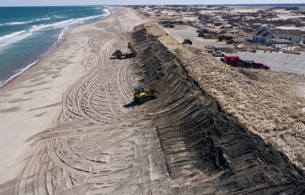 cctphoto's tweet photo. Dump trucks with the unload on the dune fronts at Sandy Neck Beach  to build them back after winter  erosion. The sand was dredged from Barnstable Harbor  and then stored in the parking lot.  It's dark color will bleach out after exposure to the sun.  @capecodtimes https://t.co/xd6vt81p8O