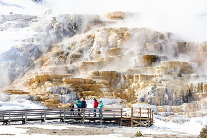 people stand on a boardwalk near a steaming hot spring