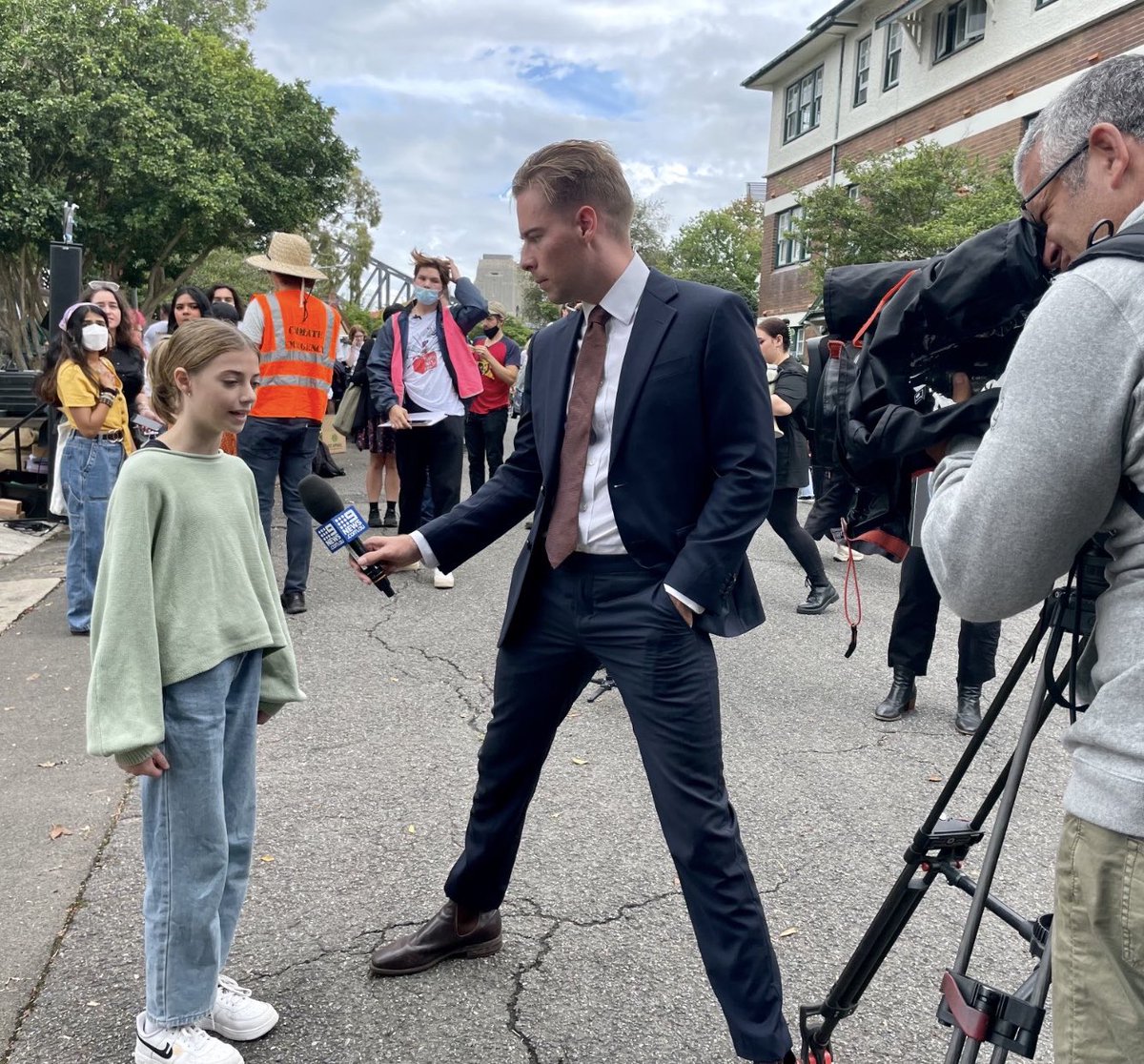 Disturbing image. BL leg posture reveals mind’s intent. Journo interviews Ella of the CC protest. There is NO REASON for this stance in front of a child .Takes up space looks larger, dominant. Draws att to genitals usually in males a sexual display. Hand in pocket. Don’t do this.