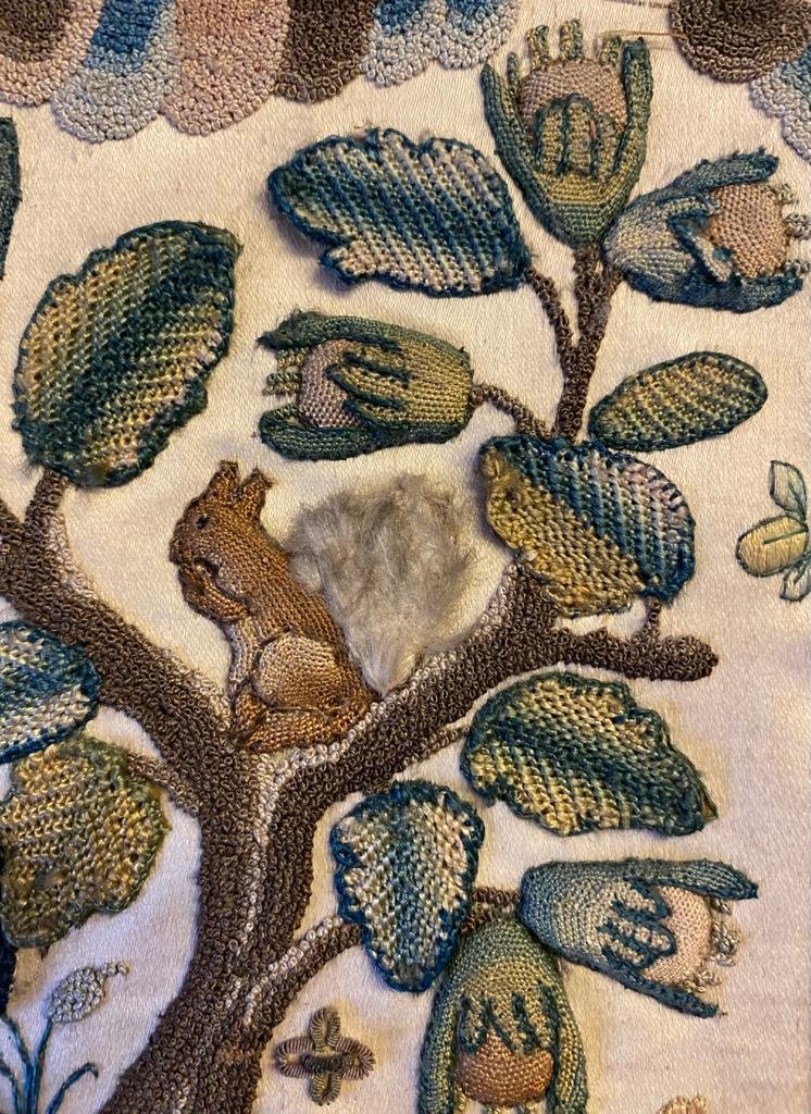 Another stunning detail from a 17th-century casket panel. The squirrel and the leaves and buds of the tree on which it perches are lightly raised. The clouds above the tree are made of tiny French knots. And the squirrel's tail is made of feathers -- a very rare survival!