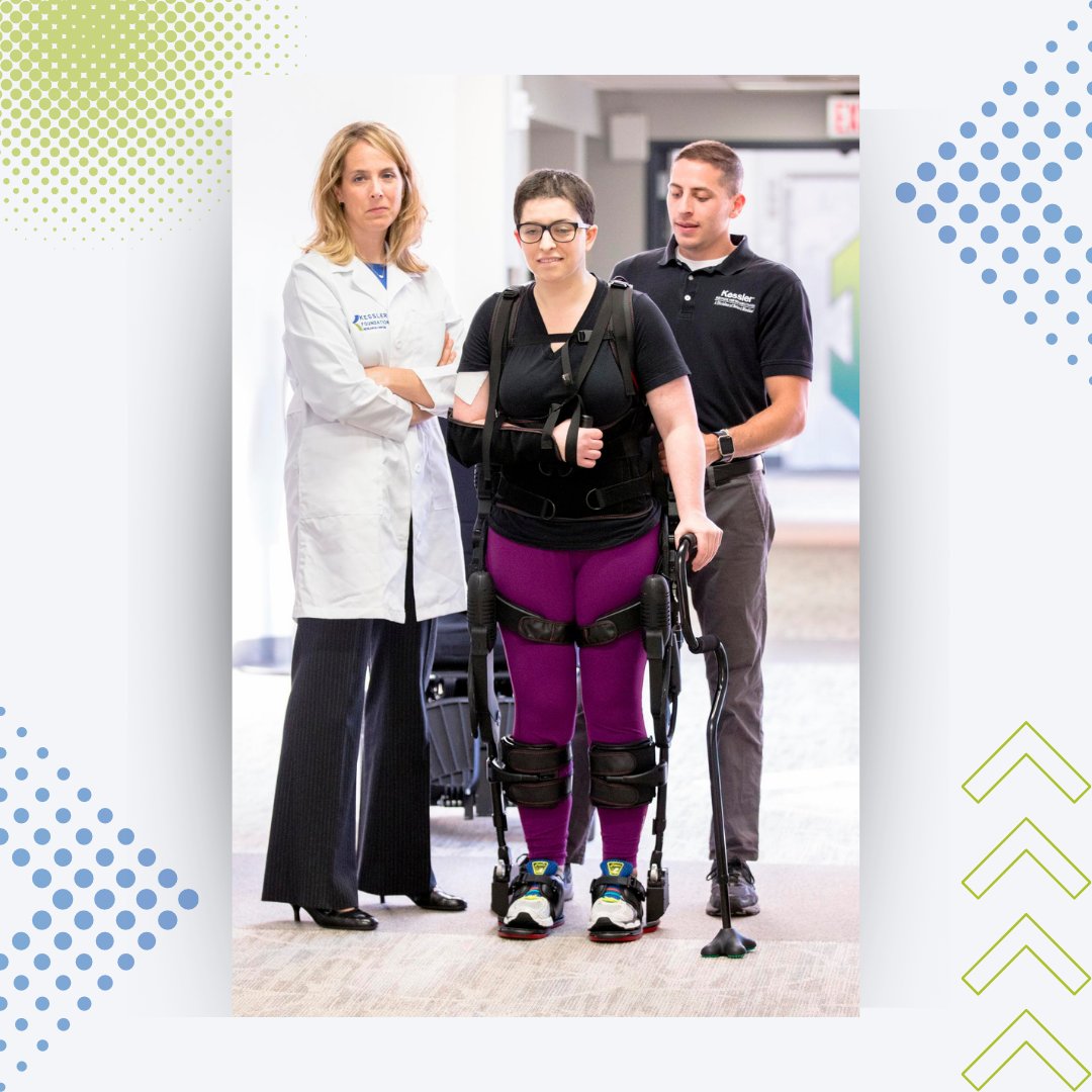 A woman is wearing the robotic exoskeleton and has her right arm in a sling. There is a physical therapist behind her and Dr. Karen Nolan is to her side. They are standing in a hallway. 