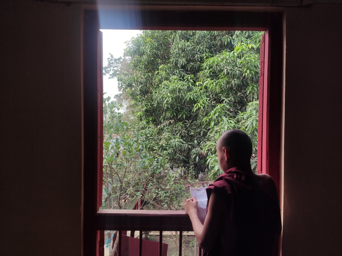 Young Buddhist monk was trying to read Buddha script with rays of sunlight inside the monastery.
