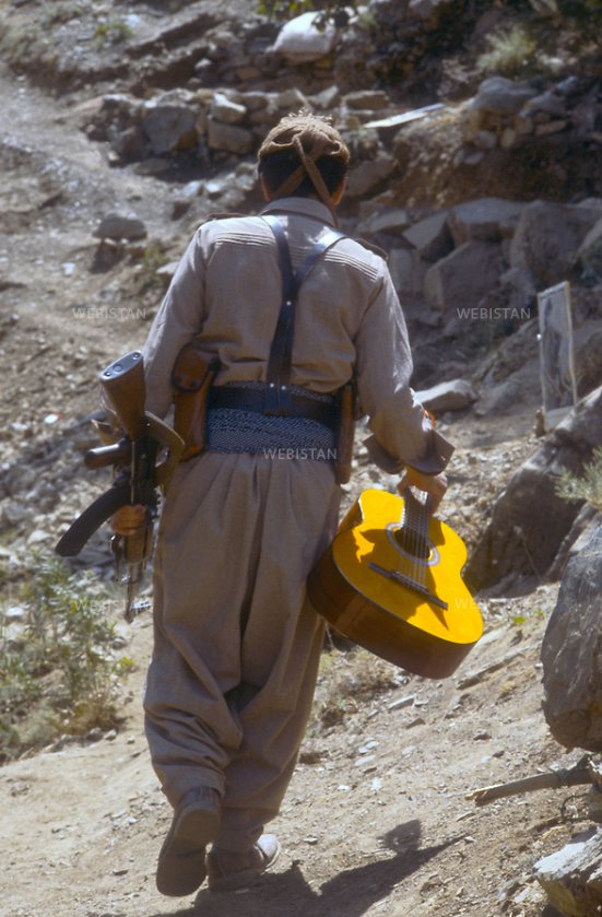 Member of the PKK, in a training camp with his weapon in one hand and his guitar in the other hand, southern Kurdistan 1980s.