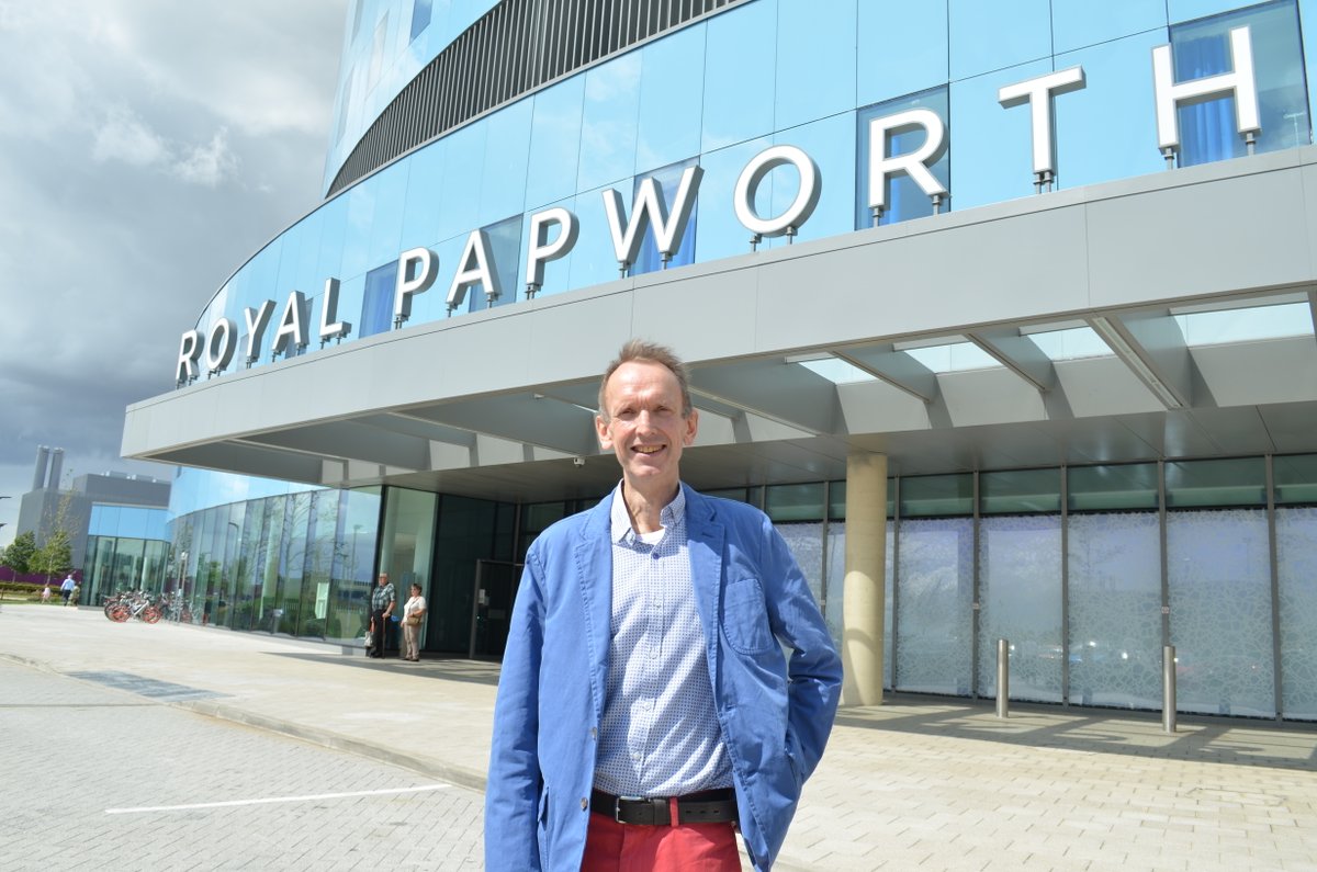 A recent photo of Richard in a blue blazer, smiling, outside a sign saying Royal Papworth Hospital