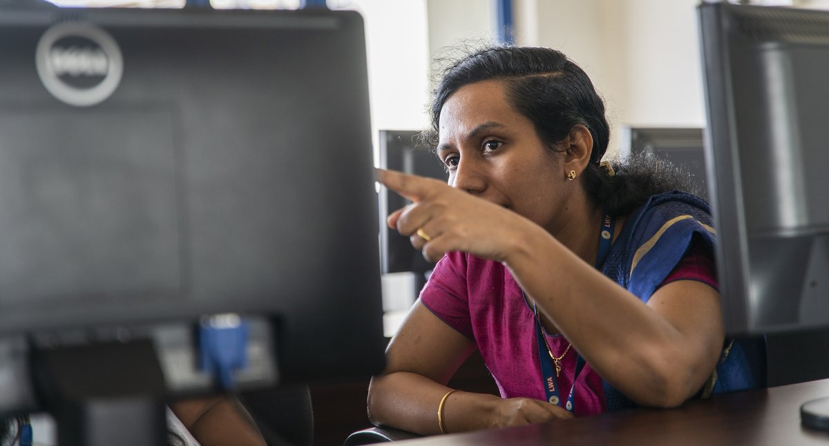 A computing teacher points at something on a computer screen.