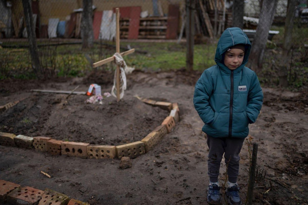 шестилетний мальчик стоит возле могилы матери, похороненной в их дворе. Буча.