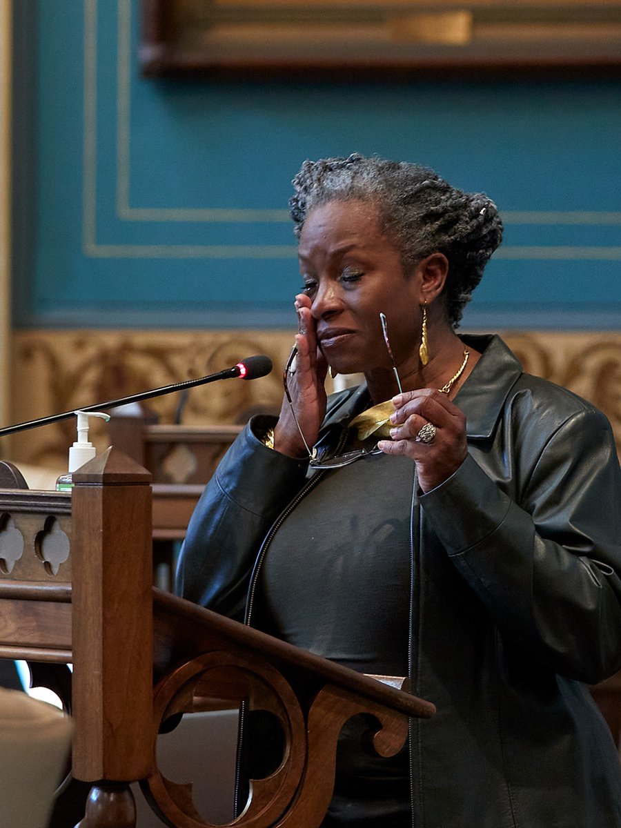 Sen. Erika Geiss holds her glasses and wipes away tears while speaking at a lectern on the MI Senate floor