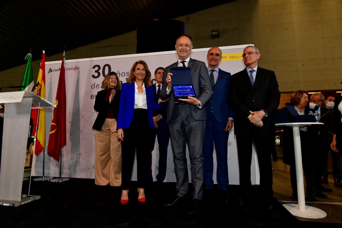 Renfe's tweet photo. 30 años del AVE: La ministra de Transportes, Movilidad y Agenda Urbana, @raquelsjimenez, entrega una placa conmemorativa a Juan Carlos Hebrero, que estrenó el nuevo servicio comercial como Supervisor de a Bordo. https://t.co/qJWsvojSSE