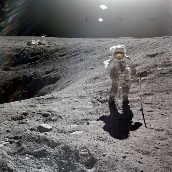 Charlie Duke in spacesuit standing by a crater on the Moon