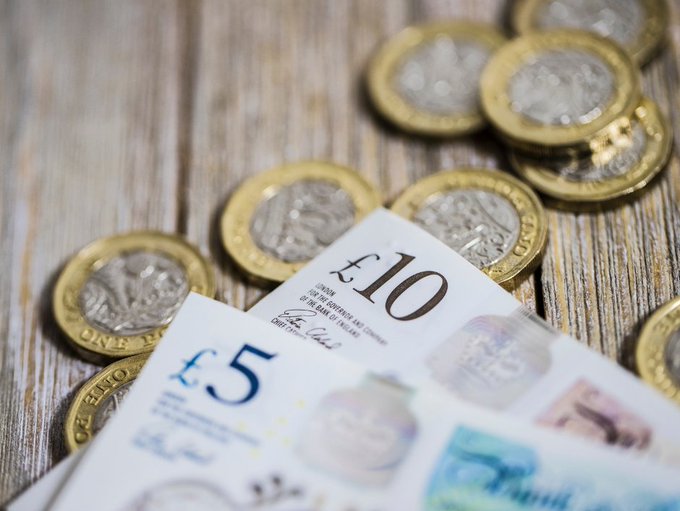 Pound coins plus five and ten pound notes shown on a wooden table