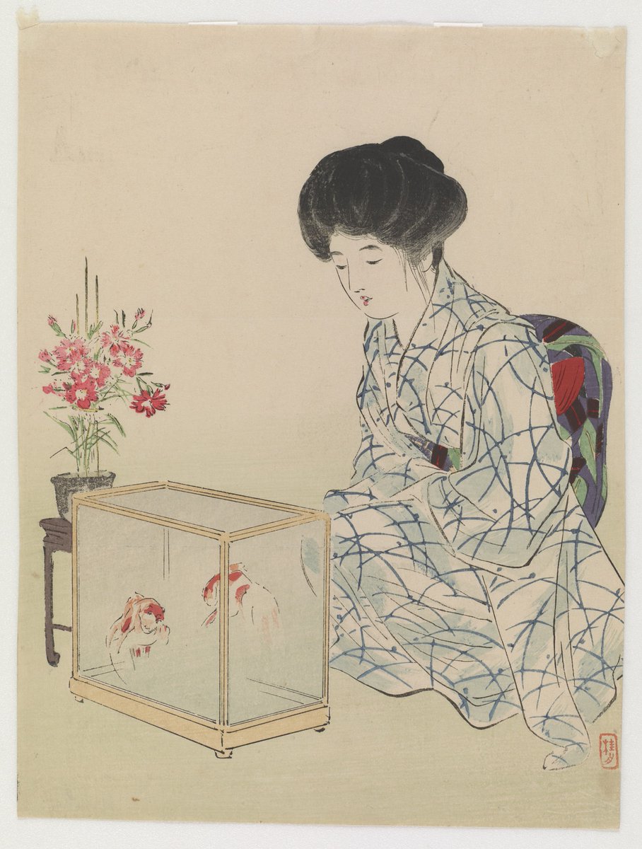 Woman seated on floor in white robe dress with blue geometric design, black hair swept into a style on top of her head. She gazes into a square aquarium in which two orange and white goldfish swim. Beside them, a vase of pink flowers.