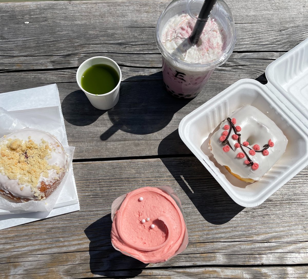 A cherry blossom doughnut, sweet iced matcha, cherry blossom cupcake, cherry blossom milk tea, and another cherry blossom doughnut sit on a wooden bench at the Wharf.