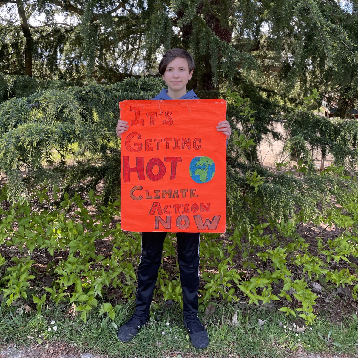 Me holding my original Climate Strike sign that I made when I was 11 years old. It reads it’s getting hot, climate action now, with a painting I made of the earth and all on a bright Orange poster board.