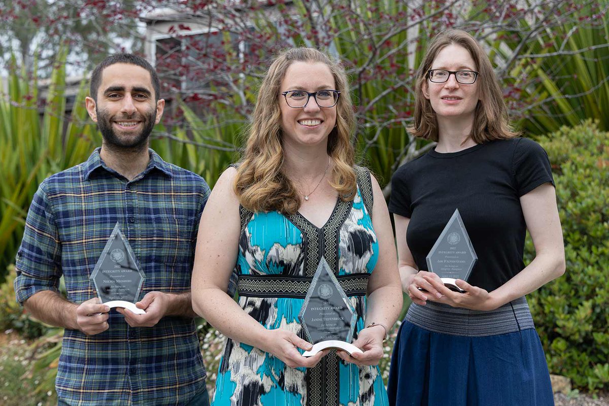A man and two women smile and hold awards in their hands.