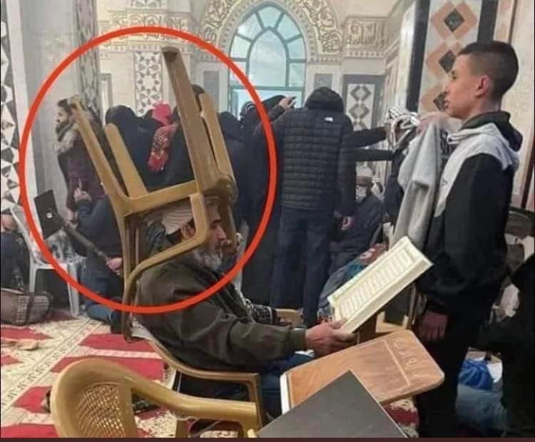 Alhamdhulillaah's tweet image. An elderly gentleman protects himself with a chair on his head as he reads the Qurʾān, while Israeli occupying forces invade Masjid al-ʾAqṣā and fire grenade and rubber bullets.