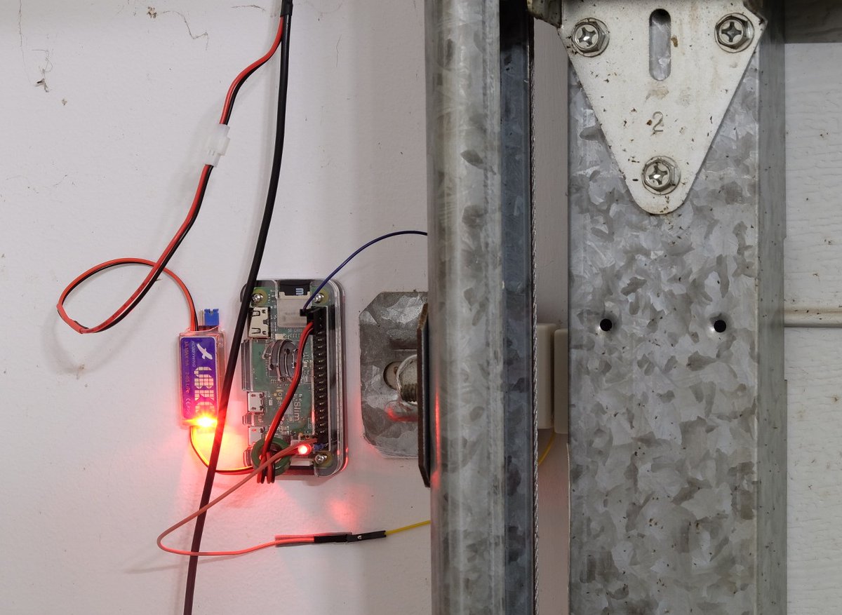Photo of the garage door monitor stuck to the wall. It has wires going to the power supply and reed switch, which is visible on the right of the photo.