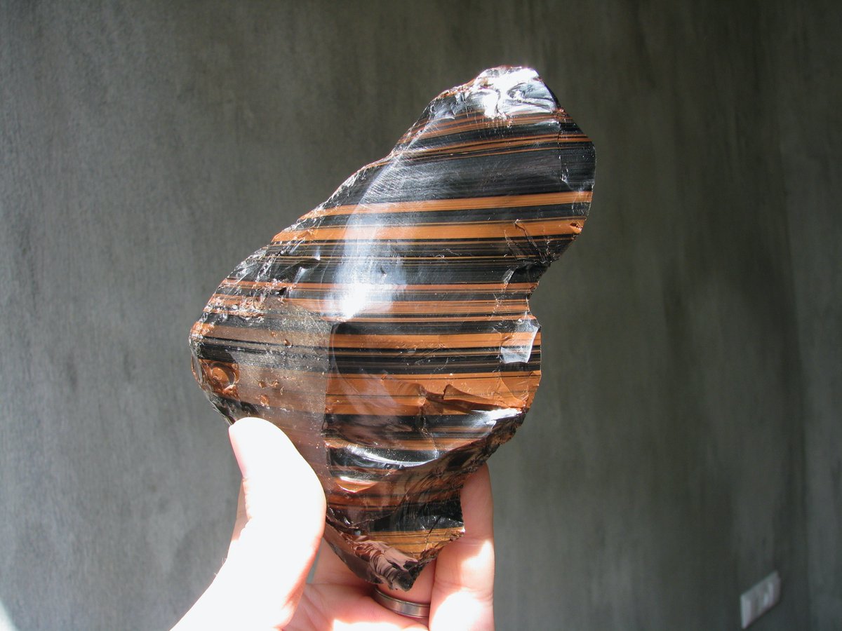 This obsidian from Armenia is striped because some of its black magnetite grains oxidized when exposed to air while still hot and became red hematite. Then the lava churned (mixing volumes with black and red grains) and stretched, like pulling taffy, creating alternating stripes.
