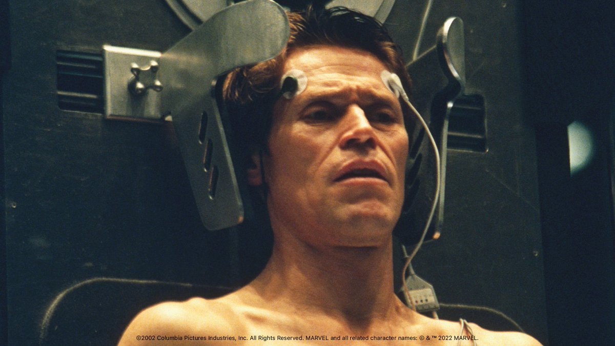 In this still, Norman Osborn (portrayed by Willem Dafoe) stands shirtless with his back against a large metal contraption, which has two protrusions halfway encircling his head. Adding to the scientific nature of the scene are two cords protruding from the device, which are stuck to his forehead with adhesive tape.