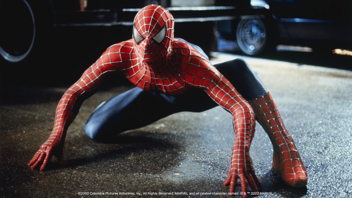 In this still, Spider-Man is dressed in his full costume and crouches on the street at night, mimicking the body position of a spider ready to spring into action.