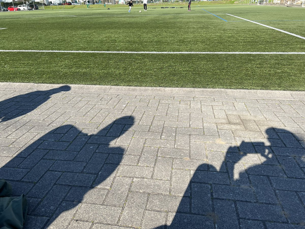 Schatten von Zuschauer*innen vor Kunstrasen.