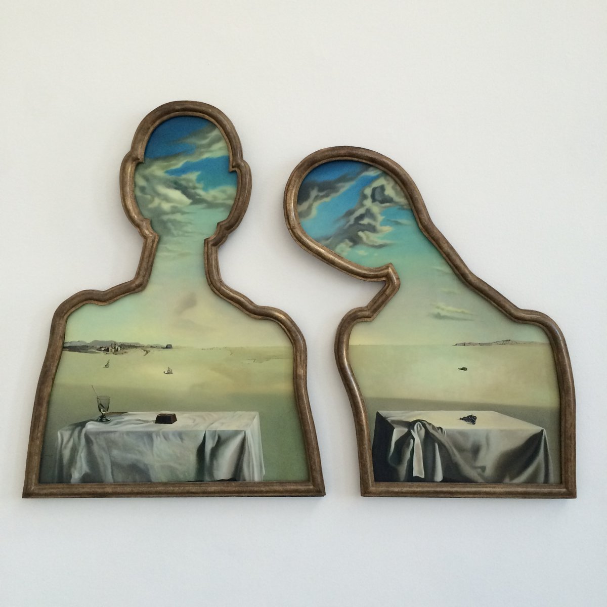 We know from remarks by #SalvadorDali himself that the cut-outs are himself and his wife Gala.

The objects on the table are repeated in an obvious visual rhyme in small figures in the landscape, then again in the landscape. 

'A Couple with Their Heads Full of Clouds'