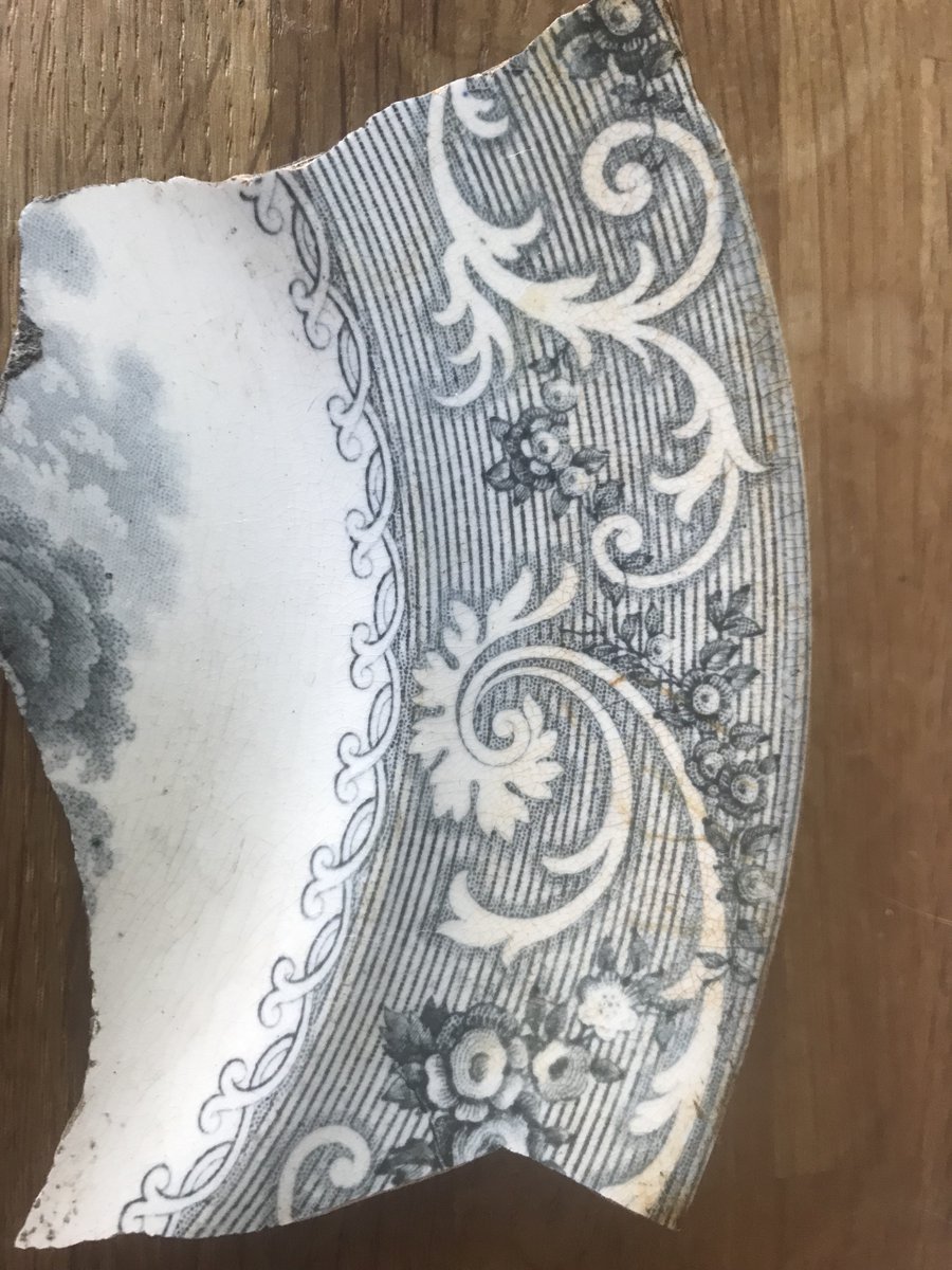 Sharing some #Britishpottery fragments from my garden, from when the house had a china shop in 1860s-70s. Fragment 1: prob dinner plate, #transferware indigo colour, scrolls and vines on the rim, centre rural scene, poss #priorypattern, cloudy trees