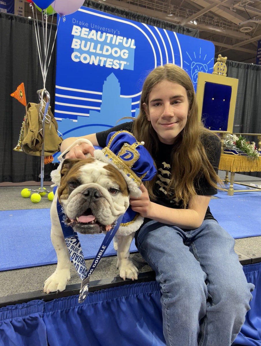 Gideon sitting on a stage to the right of a Bulldog wearing a medal and a crown (Bam Bam). Bam Bam looks like royalty.