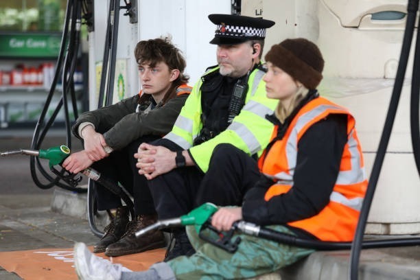 dearaunty's tweet photo. Has the Policeman joined the protestors? - Is he waiting for a van to put them in? - Why is he sitting with them, rather than arresting them? https://t.co/W5PzRG8Oo9