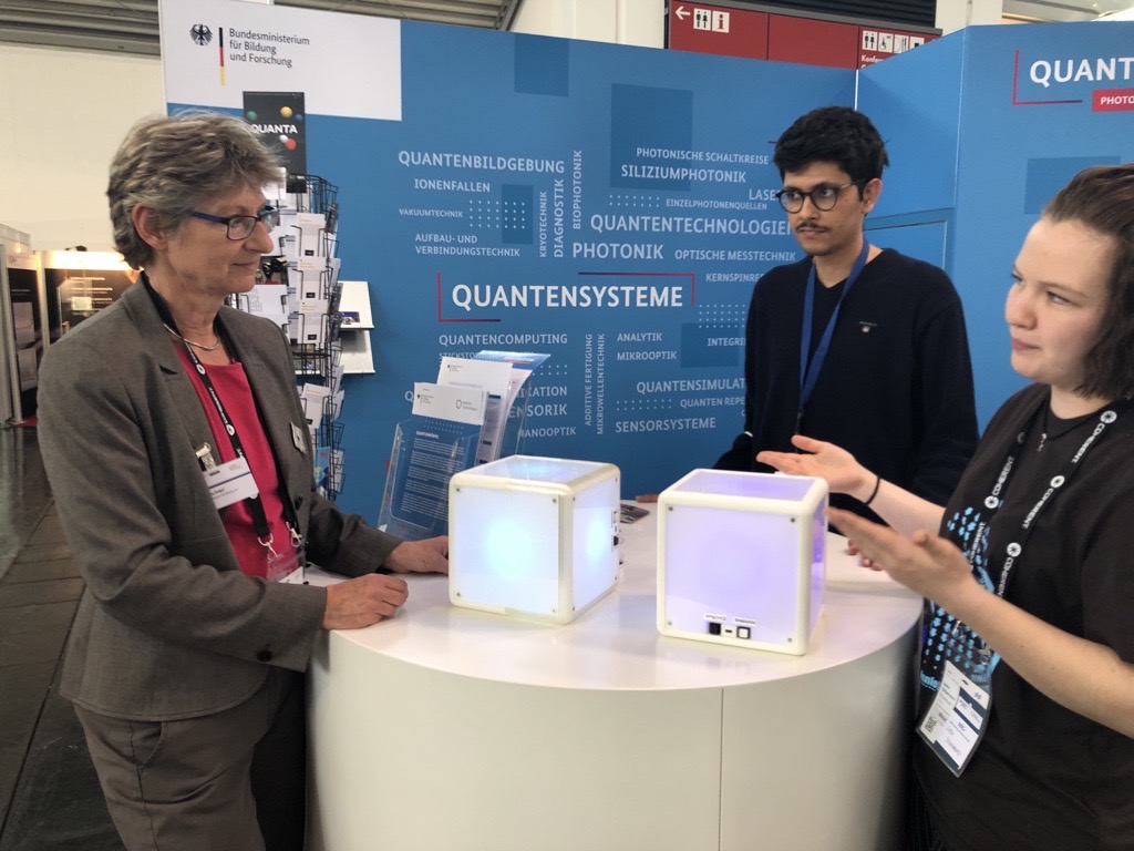 QuantenTech's tweet photo. Zum Abschluss der @PHOTONICSWORLD hat sich Ulrike Geiger vom @BMBF_Bund die spannenden Exponate an unserem Stand erklären lassen: Ein Kryostat und einen Quantenprozessor aus dem Förderprojekt #QExa und Quantenwürfel zur Veranschaulichung von Verschränkung aus dem Projekt #QUANTA. https://t.co/F7xZ4Q7jO3