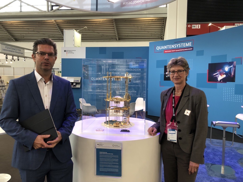 QuantenTech's tweet photo. Zum Abschluss der @PHOTONICSWORLD hat sich Ulrike Geiger vom @BMBF_Bund die spannenden Exponate an unserem Stand erklären lassen: Ein Kryostat und einen Quantenprozessor aus dem Förderprojekt #QExa und Quantenwürfel zur Veranschaulichung von Verschränkung aus dem Projekt #QUANTA. https://t.co/F7xZ4Q7jO3
