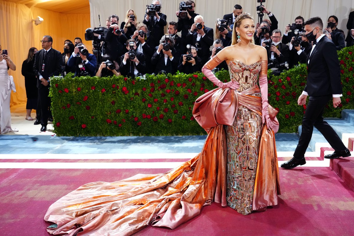 harpersbazaarus's tweet photo. Blake Lively went all-in on the dress code in Atelier Versace. A bustle! Opera gloves! Salmon pink! (With an Art Deco column under all that wrapping; the clashing of different eras of fashion seems to be a #MetGala theme.) But wait... it's not just pink...it's unfurls into blue! https://t.co/ZGfIPpLCH4