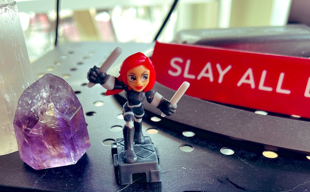 An amethyst crystal, a Black Widow super hero figure and a sign that says ‘slay all day’.