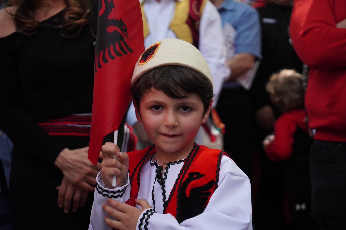 A young boy smiles for the camera. He is wearing traditional Albanian garb.