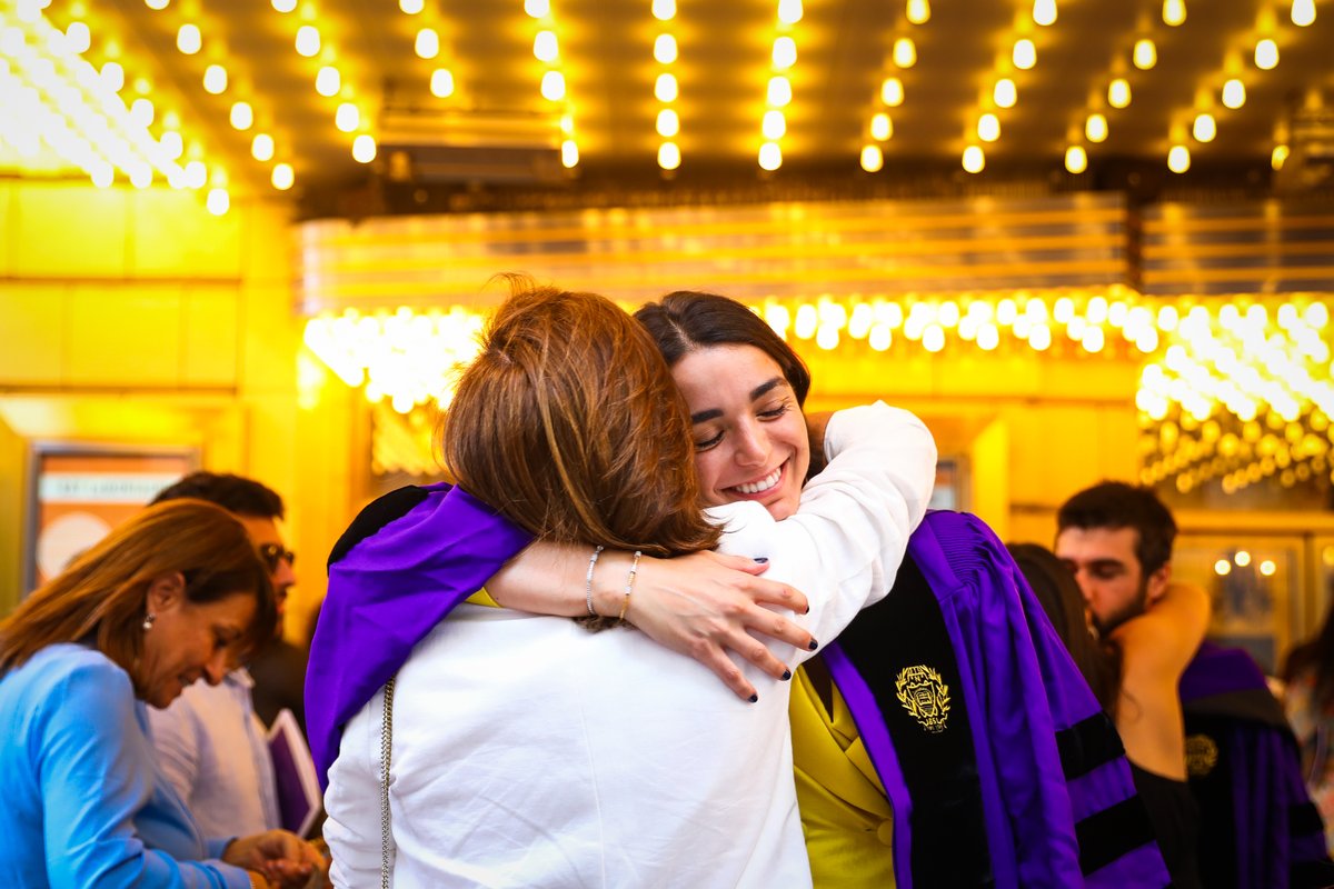 a graduate hugs a loved one under the lights of the chicago theatre marquee